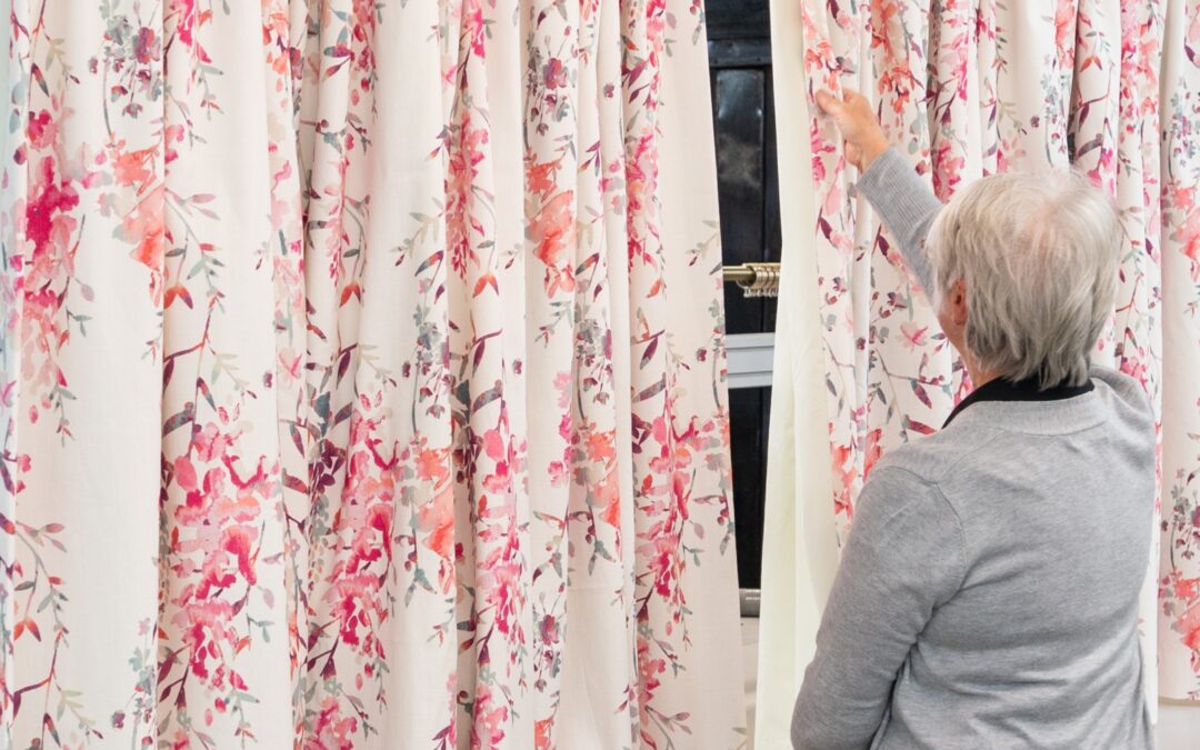 Person inspecting handmade floral curtains with a pinch pleat heading in a bespoke curtain workshop