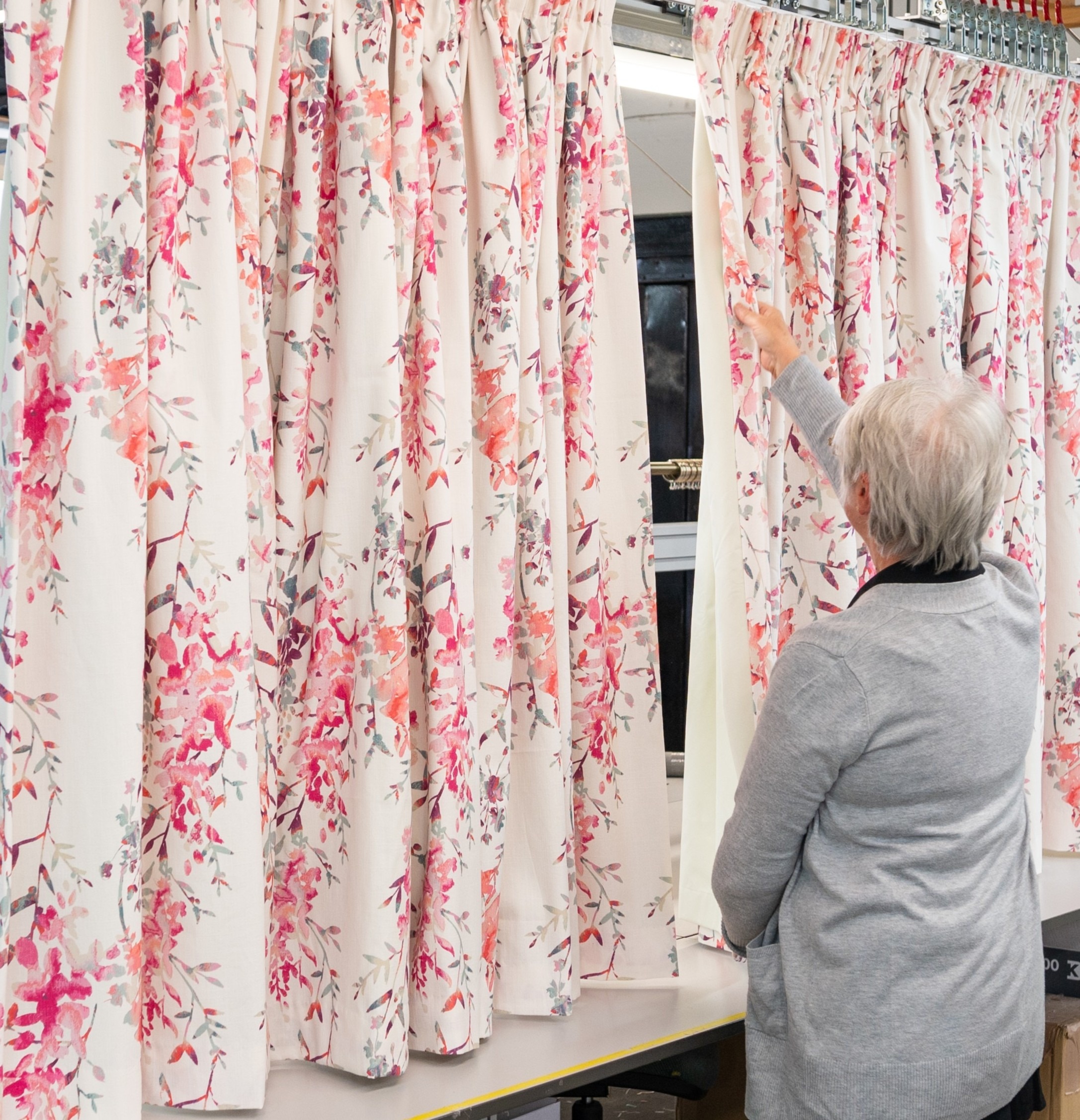 Person inspecting handmade floral curtains with a pinch pleat heading in a bespoke curtain workshop
